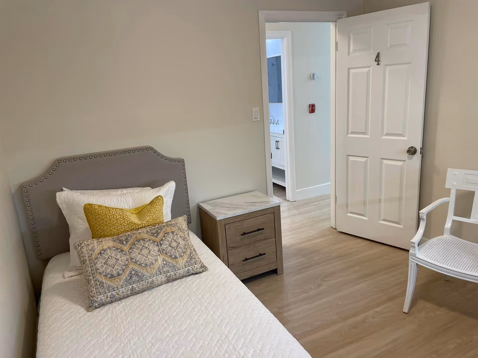 A bedroom in a senior care facility with a bed, nightstand, and open doorway.