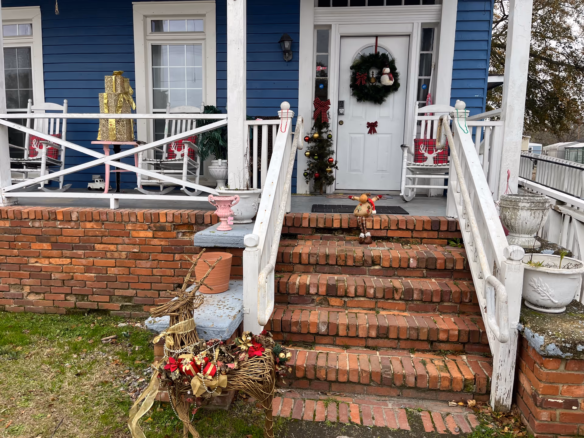 Front porch of a blue house with white railings, brick steps, and Christmas decorations.