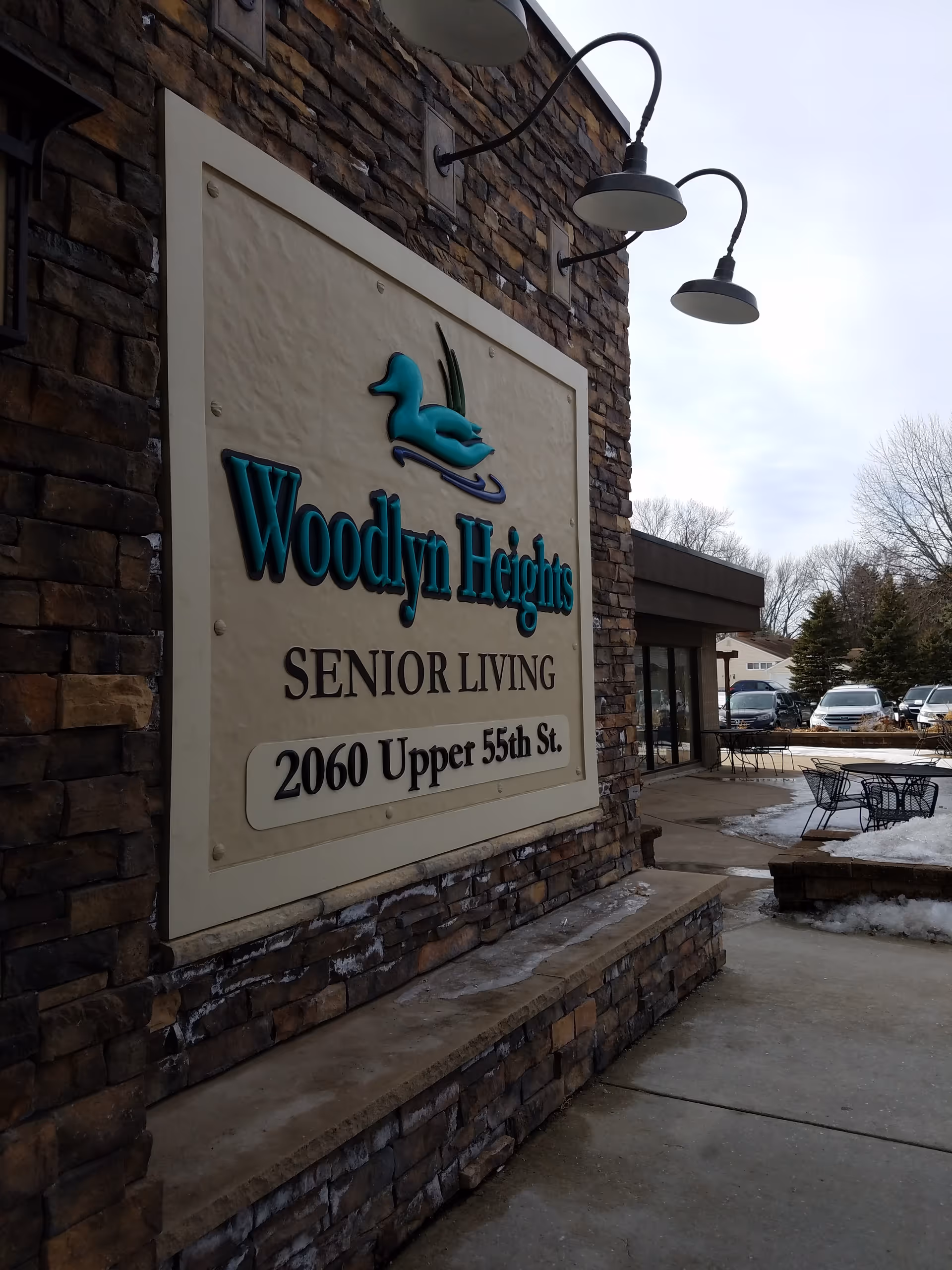 Exterior view of Woodlyn Heights Senior Living with a large stone sign and outdoor seating.
