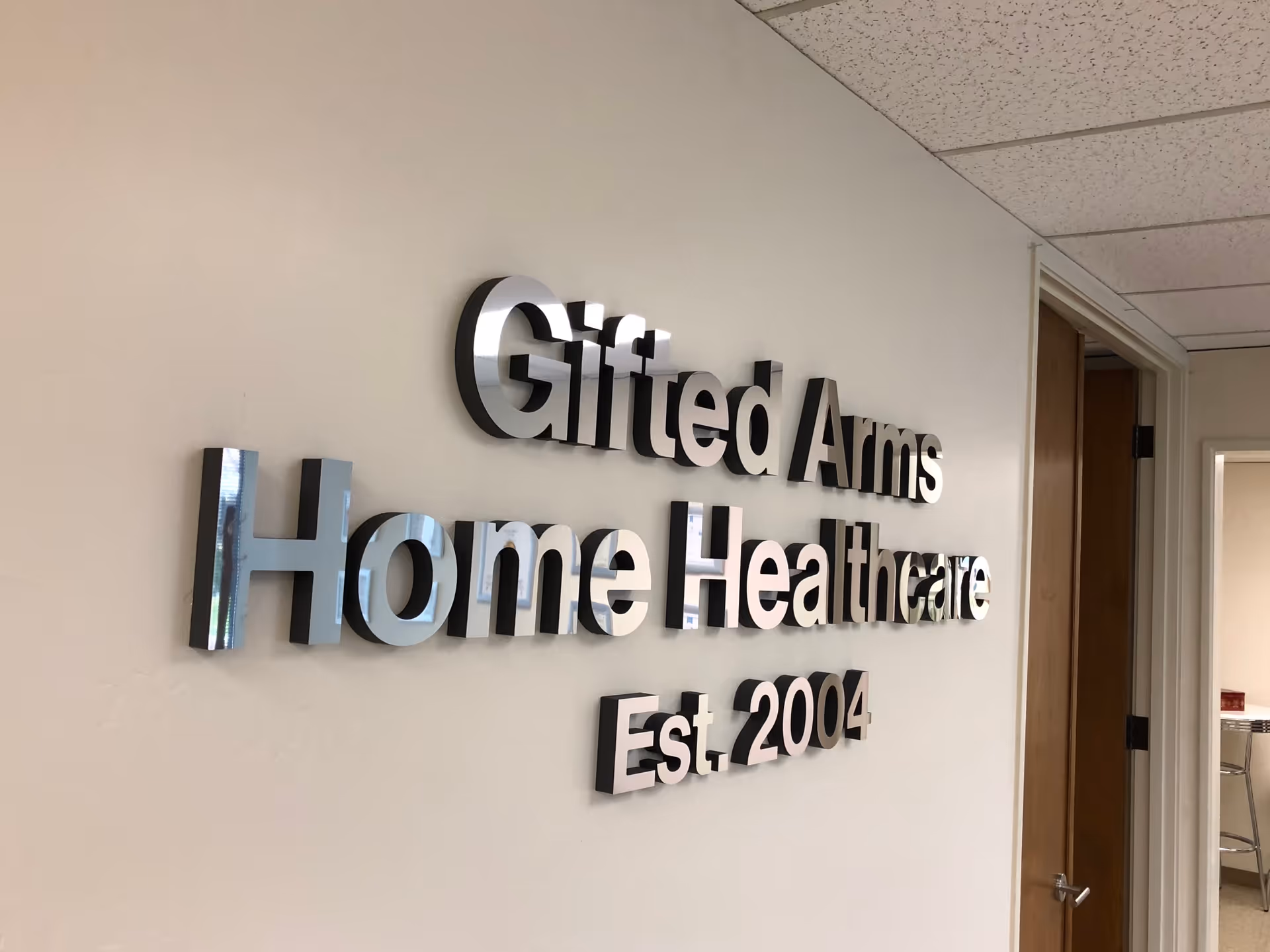 Indoor wall with a large metal sign reading Gifted Arms Home Healthcare Est. 2004
