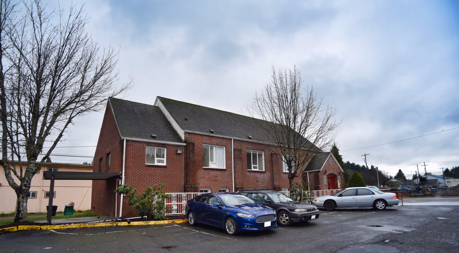 Exterior brick clinic building with a parking lot and bare trees under cloudy sky.