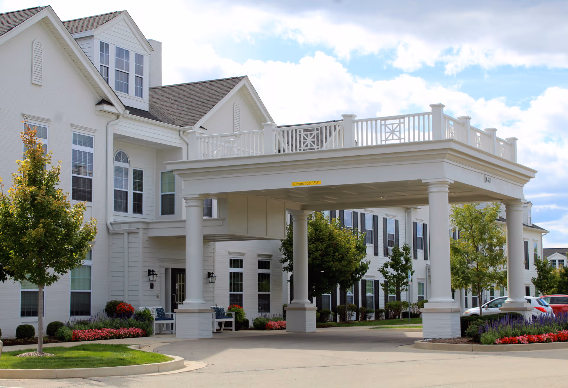White senior living building with a large porte-cochère and landscaped entrance.