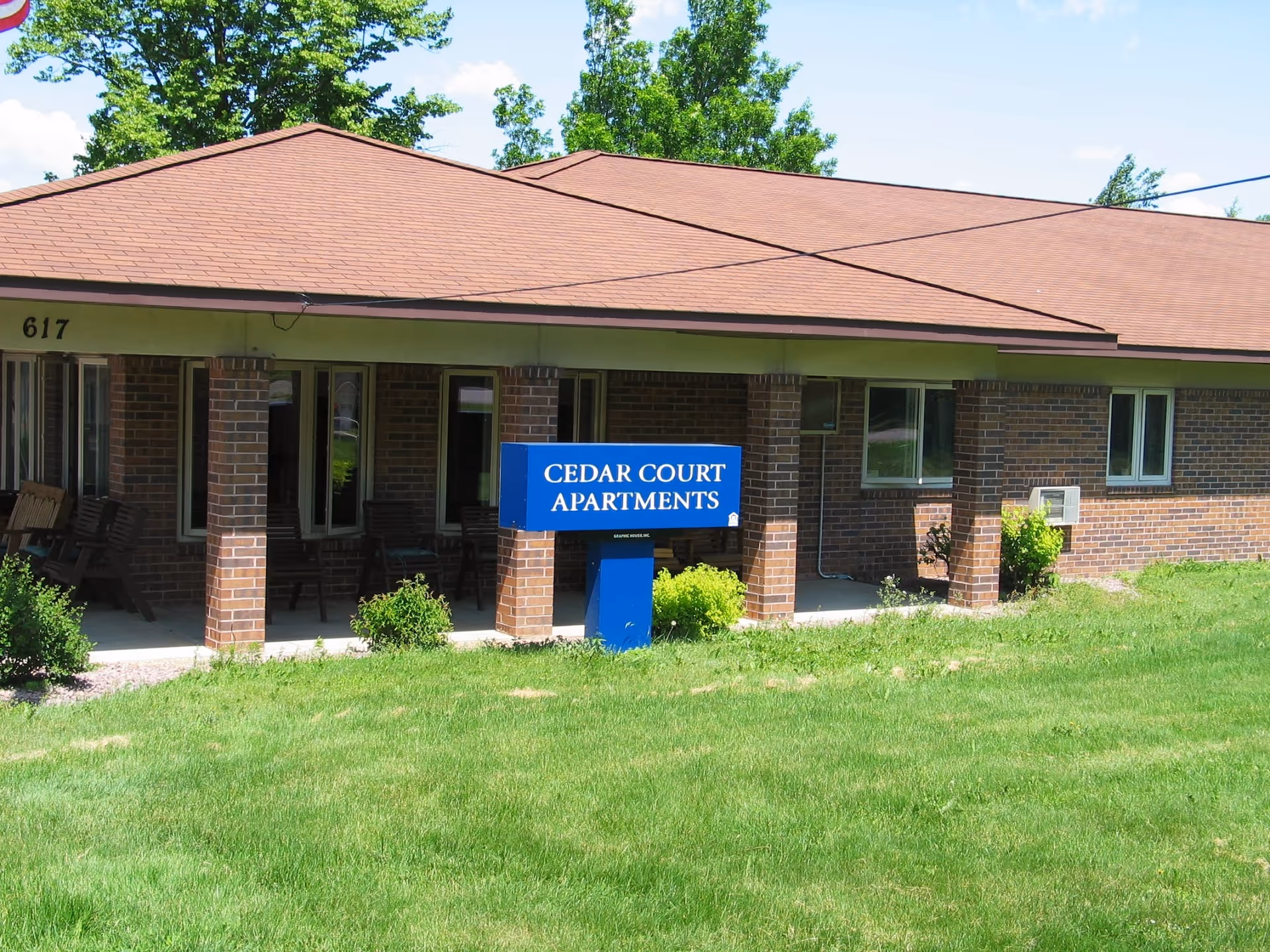 Brick, single-story building with a blue Cedar Court Apartments sign and green lawn.