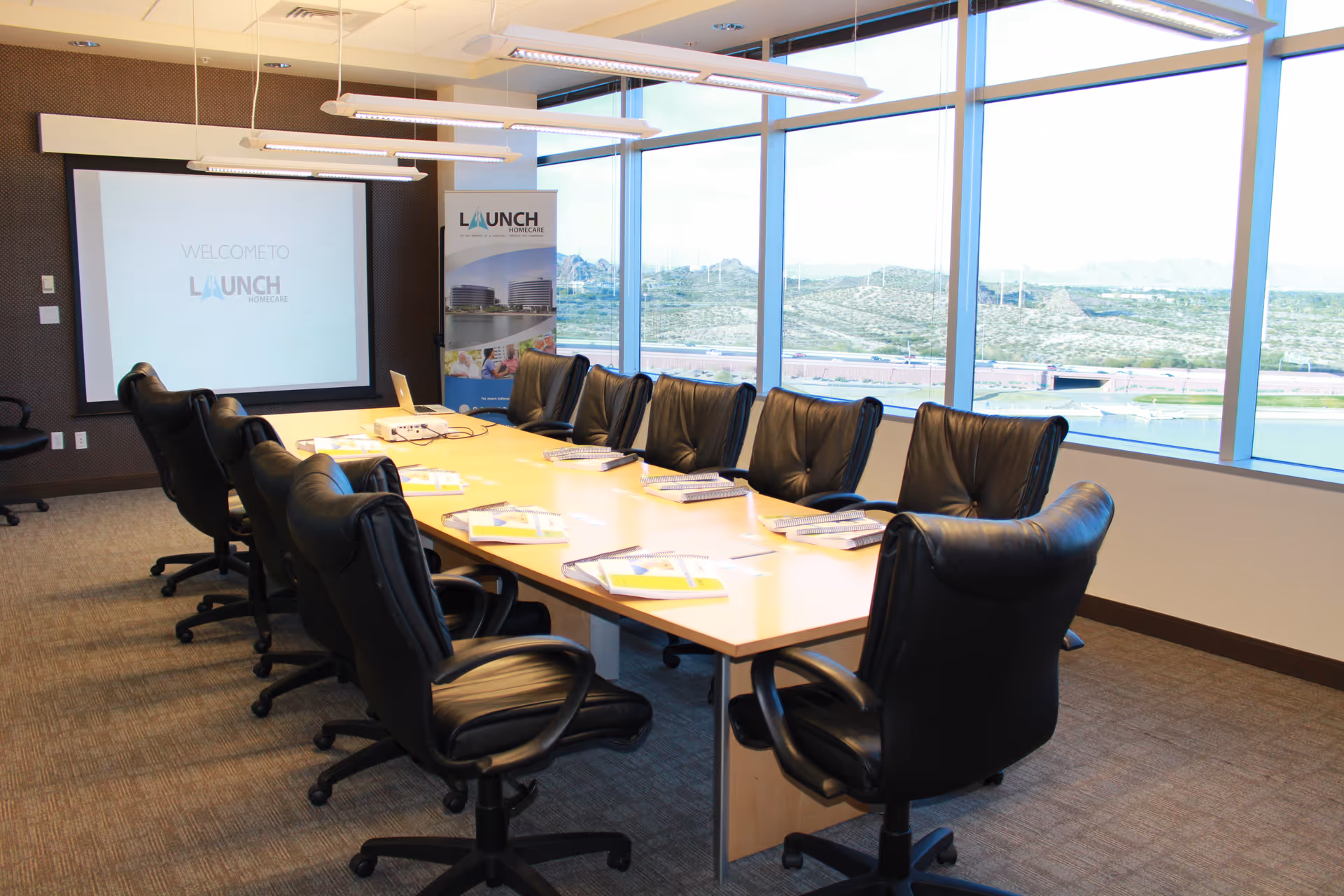 A conference room with a long wooden table, black leather chairs, and a projector screen.