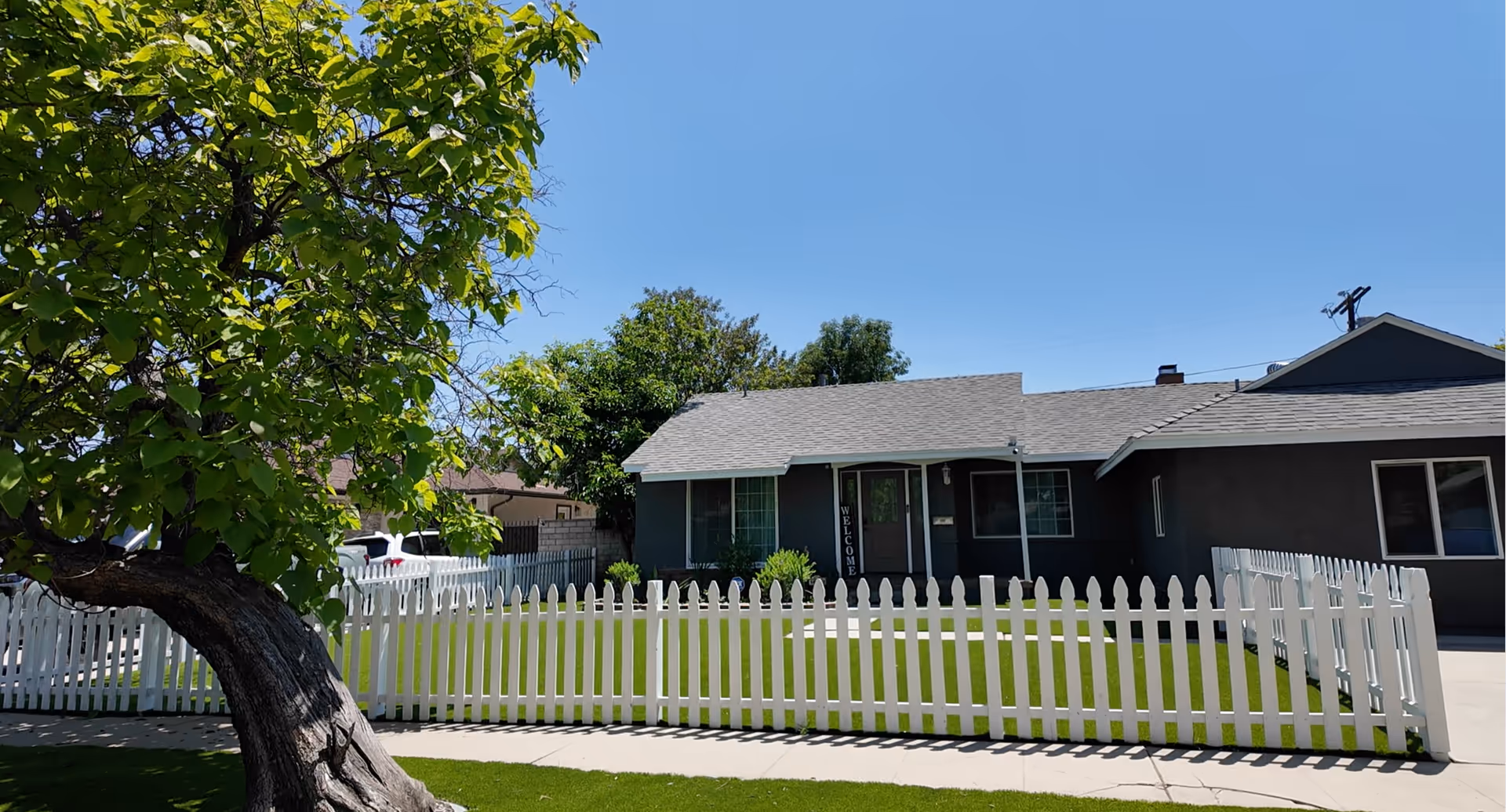 A single-story blue-gray building with a white picket fence and green lawn.