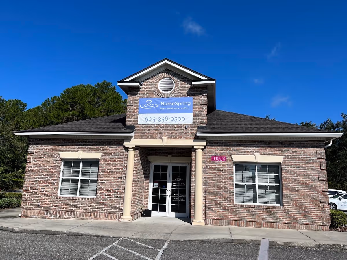 Brick nursing facility front with NurseSpring sign and glass entrance amid blue sky.