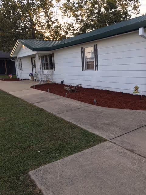 White single-story building with green roof, front walkway, and red mulch landscaping.