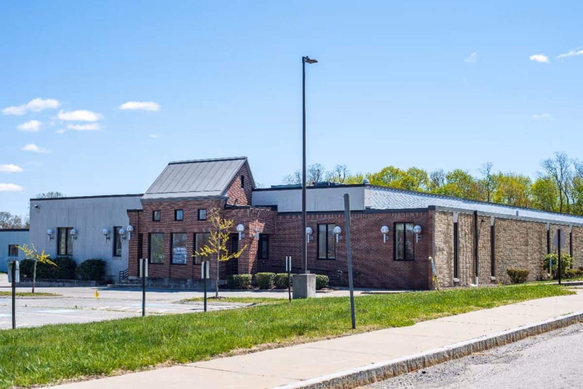 Brick senior living facility with a parking lot, walkway, and clear blue sky.