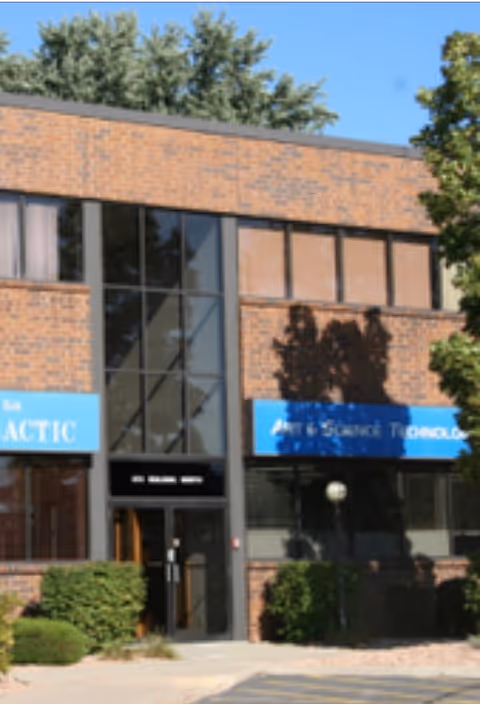 Brick storefront building with glass entrance, blue signs, and trees outside.
