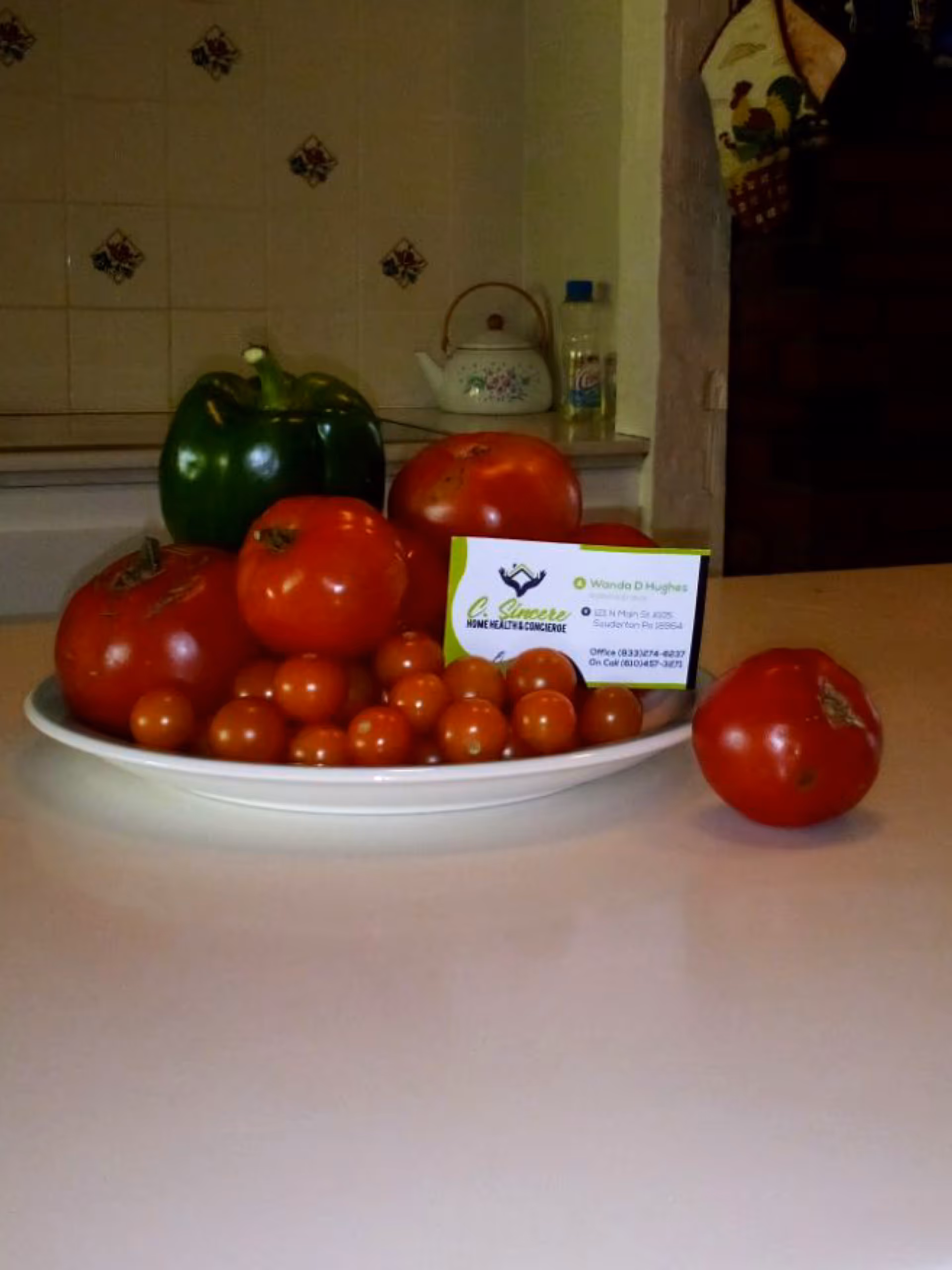 Plate of tomatoes and a green pepper on a kitchen counter with a business card.