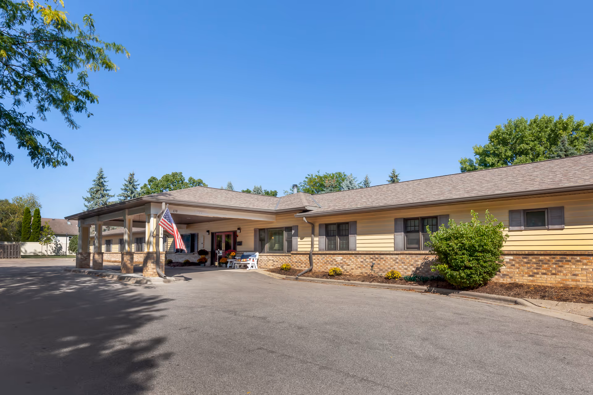 Exterior of Brookdale Sun Prairie, a single-story senior living facility with entrance, flag, and landscaping.