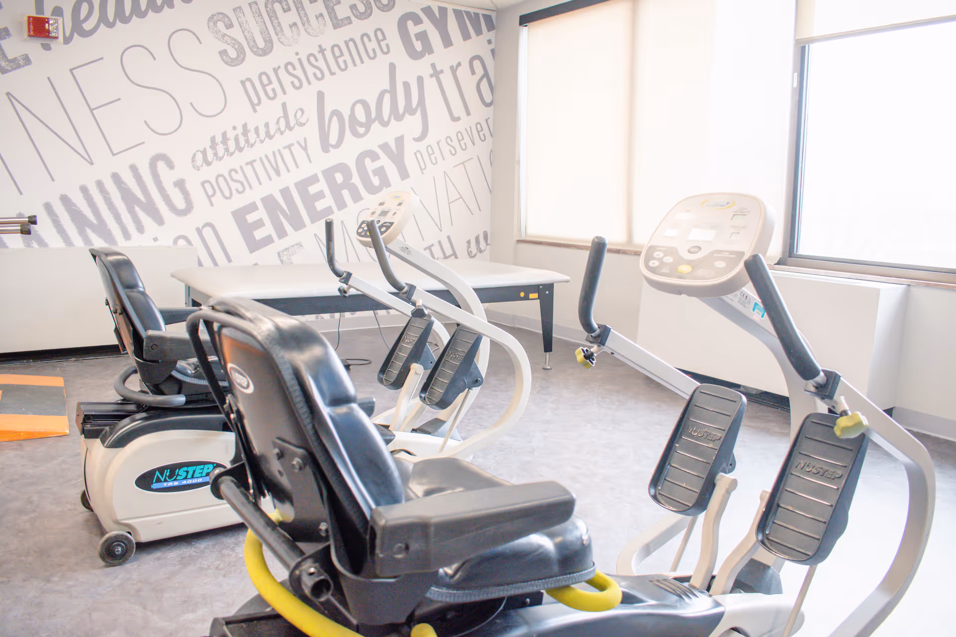 Bright fitness room with recumbent exercise machines and motivational word art on the wall.