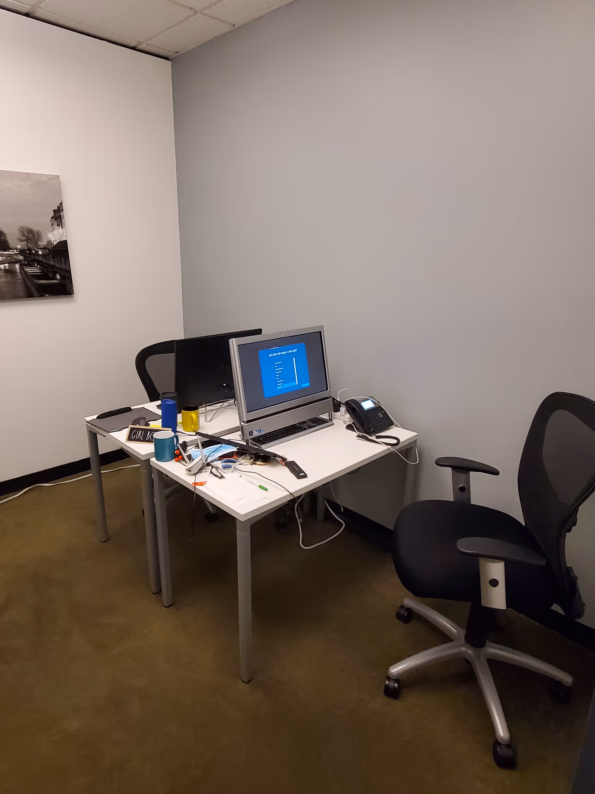 Small office desk with a computer, phone, and chair in a plain interior room.