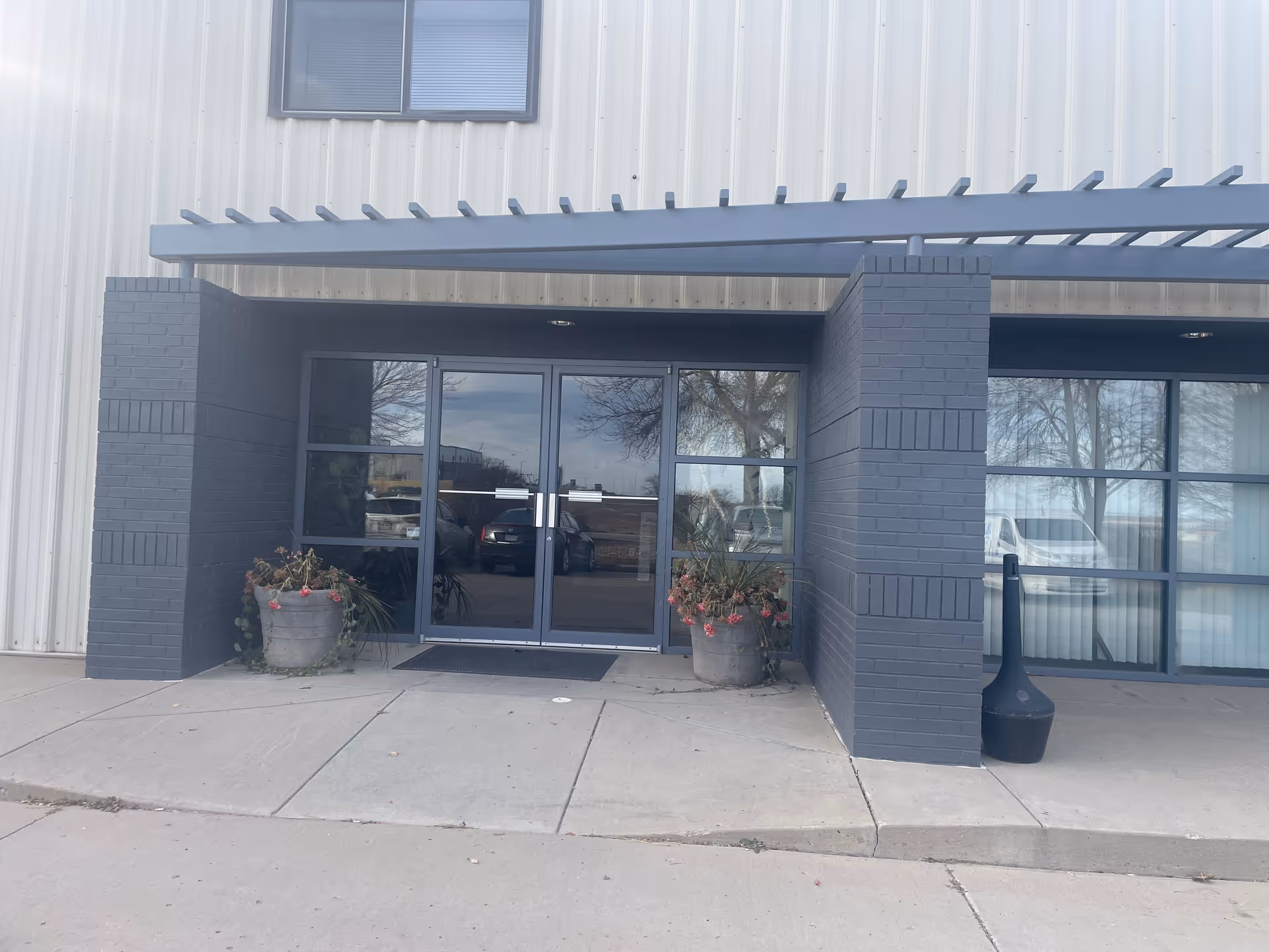 Modern building entrance with glass doors, brick columns, overhang, and potted plants.