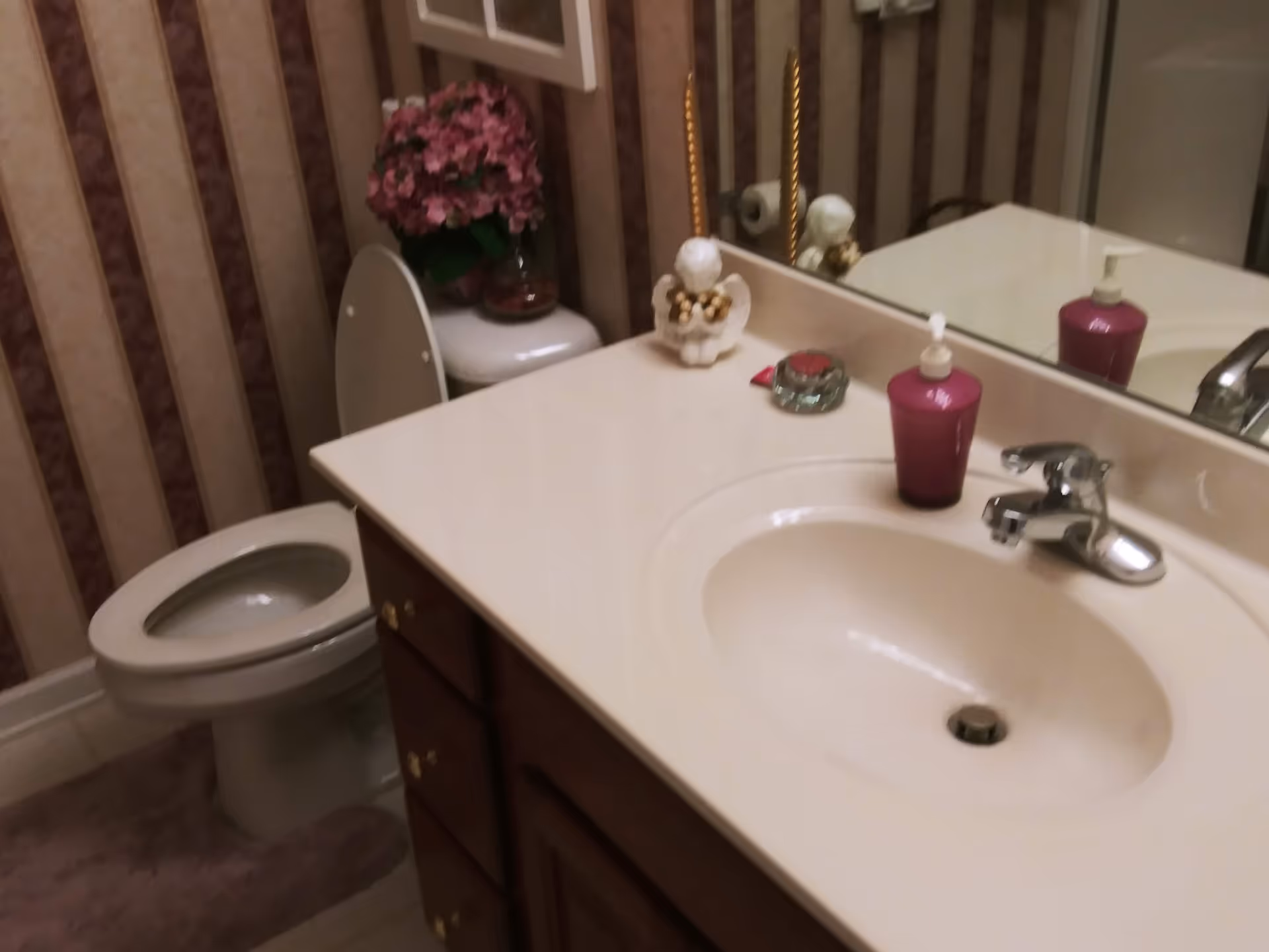 Bathroom with sink, mirror, toilet, purple soap dispenser, and floral decor.