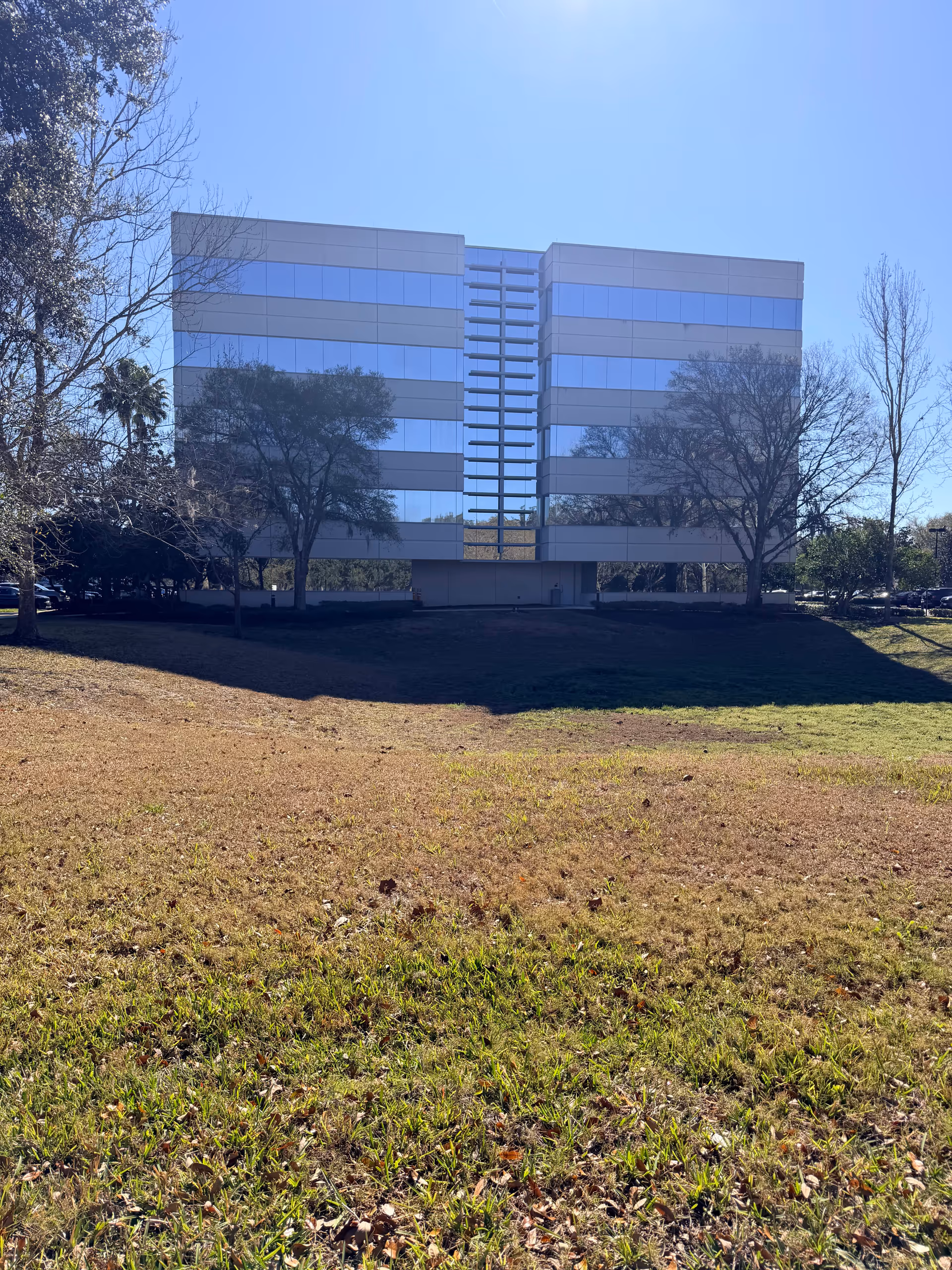Modern, glass-front building with a grassy foreground and leafless trees.