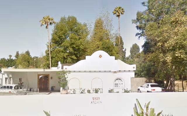 Exterior view of a white building with arches, parked cars, and palm trees.