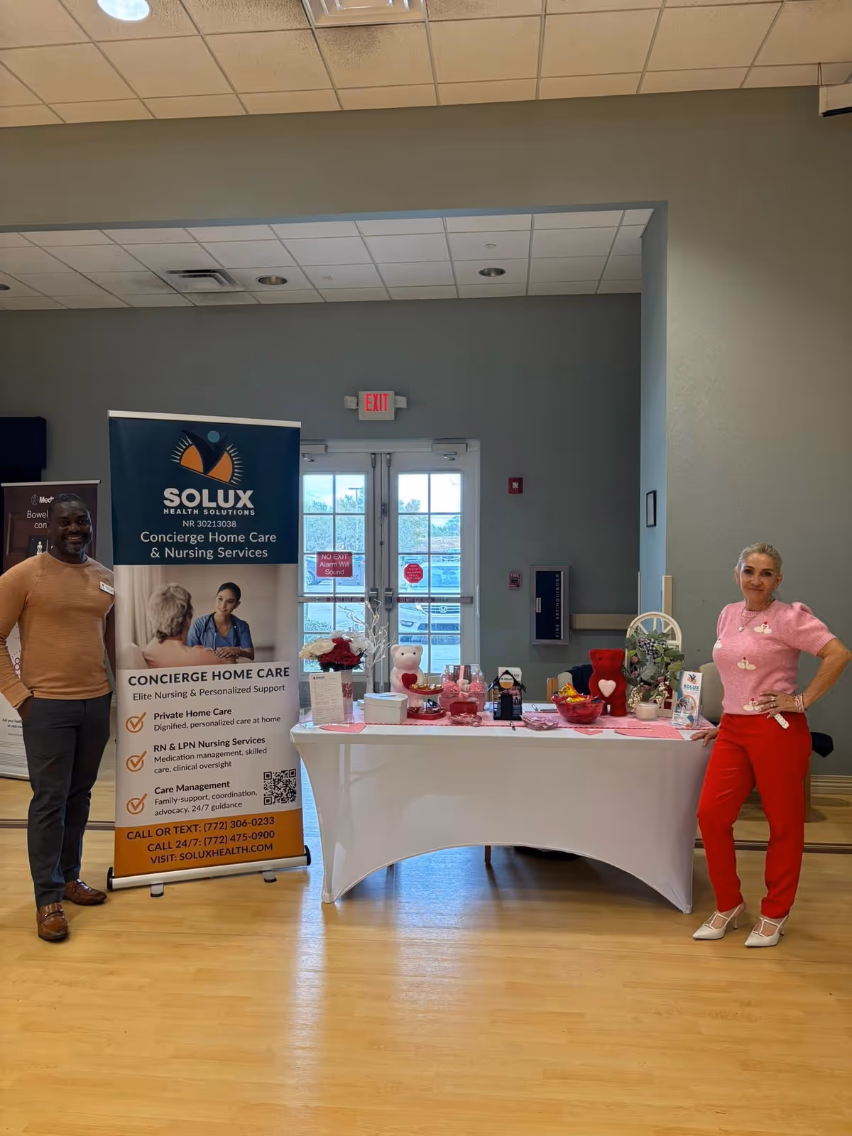 Two staff members stand beside a Solux Health Solutions banner and a table indoors.