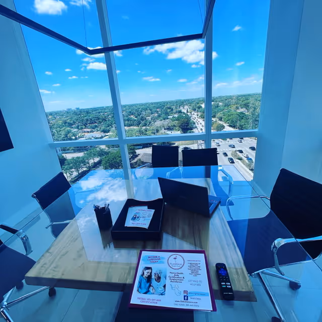 Bright glass-walled conference room with a wooden table, laptop, and cityscape view.