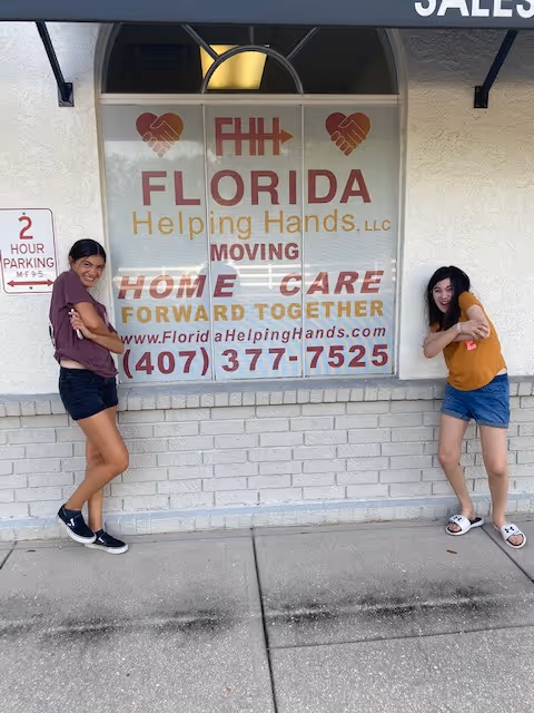 Two girls pose beside a Florida Helping Hands storefront sign on the building exterior