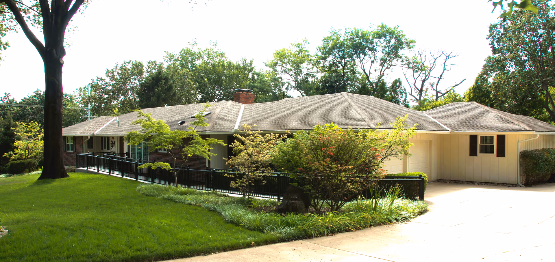 Single-story senior living facility exterior with a ramp, driveway, and manicured landscaping.