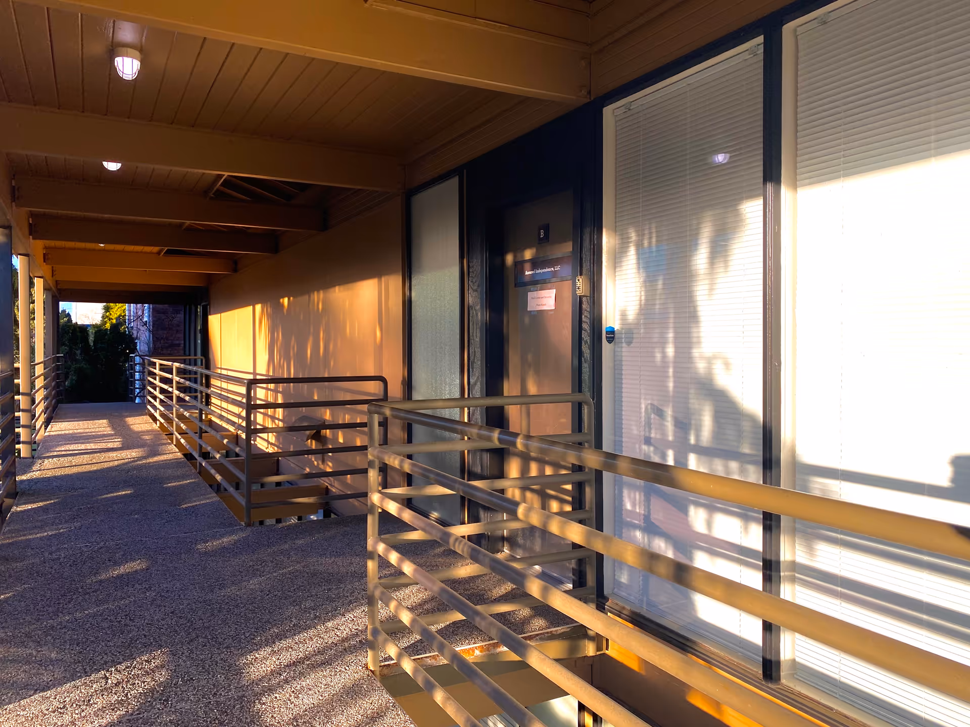 Outdoor walkway along a beige building with metal railings and sunlit shadows.