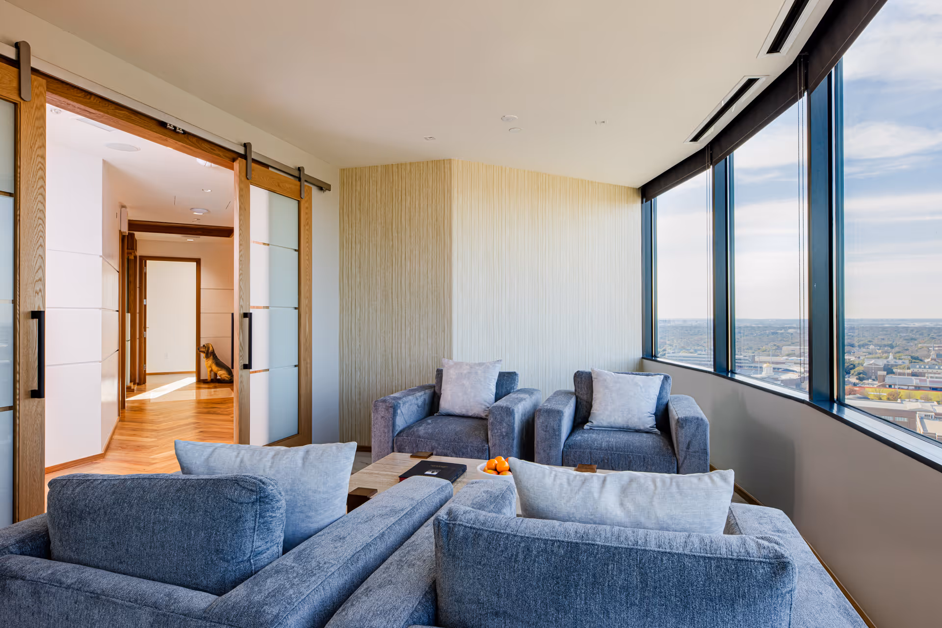 Lounge area with gray seating and floor-to-ceiling windows offering city views.
