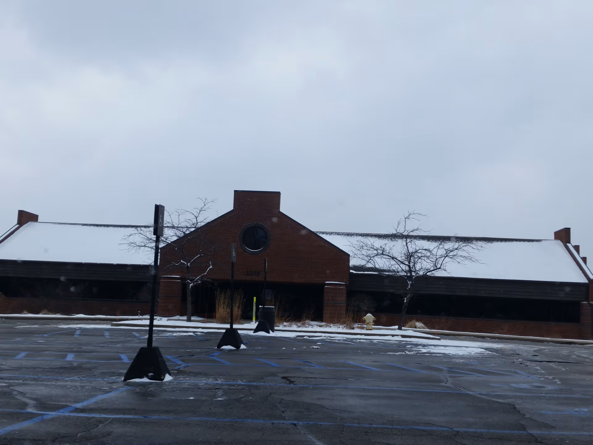 Snow-covered brick building exterior with a circular window and empty parking lot.