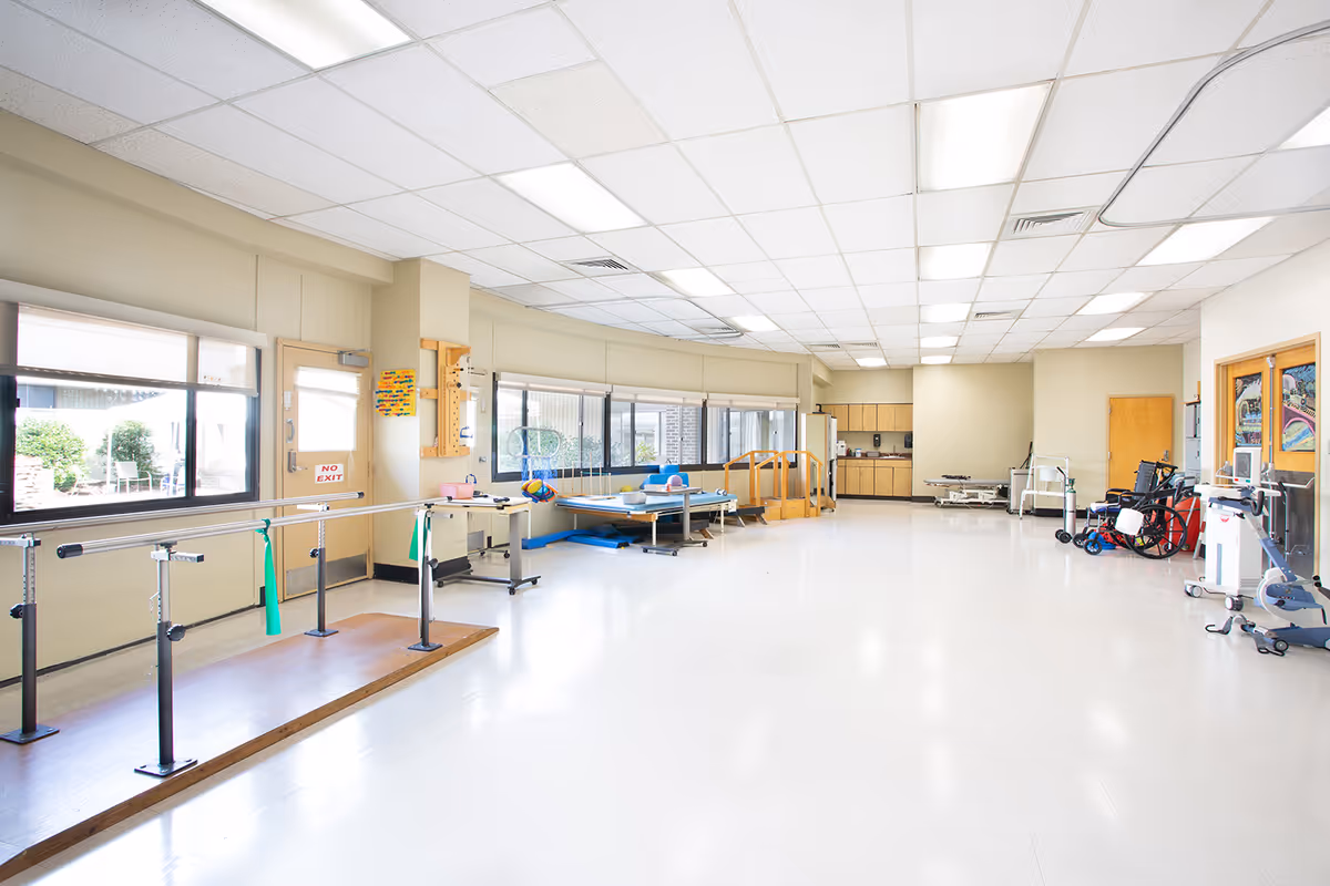 Bright therapy gym with parallel bars, mats, wheelchairs, and mobility equipment in a spacious room