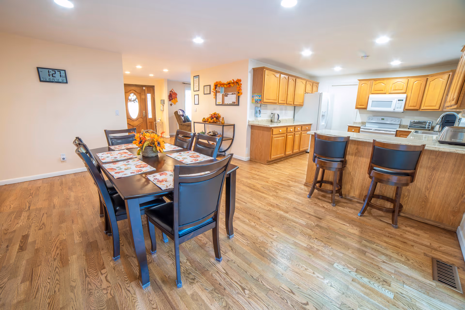 Bright dining room with a long table, chairs, and an open kitchen in the background.