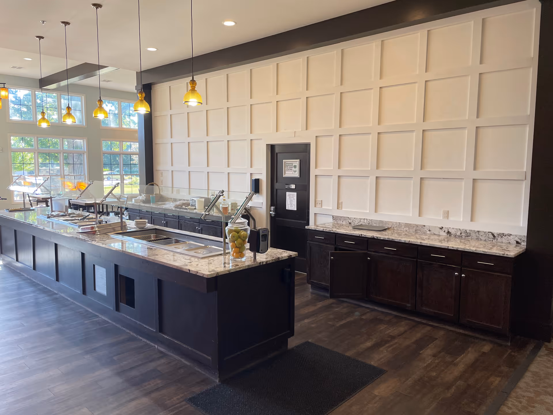 Long dining area with serving stations, marble countertops, and pendant lights.
