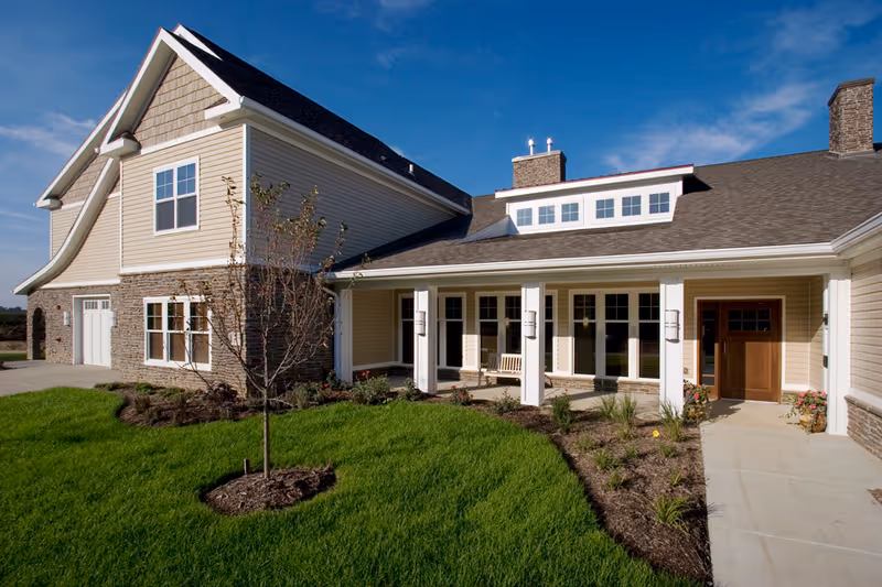 Exterior view of a senior living facility with a manicured lawn and covered entrance.