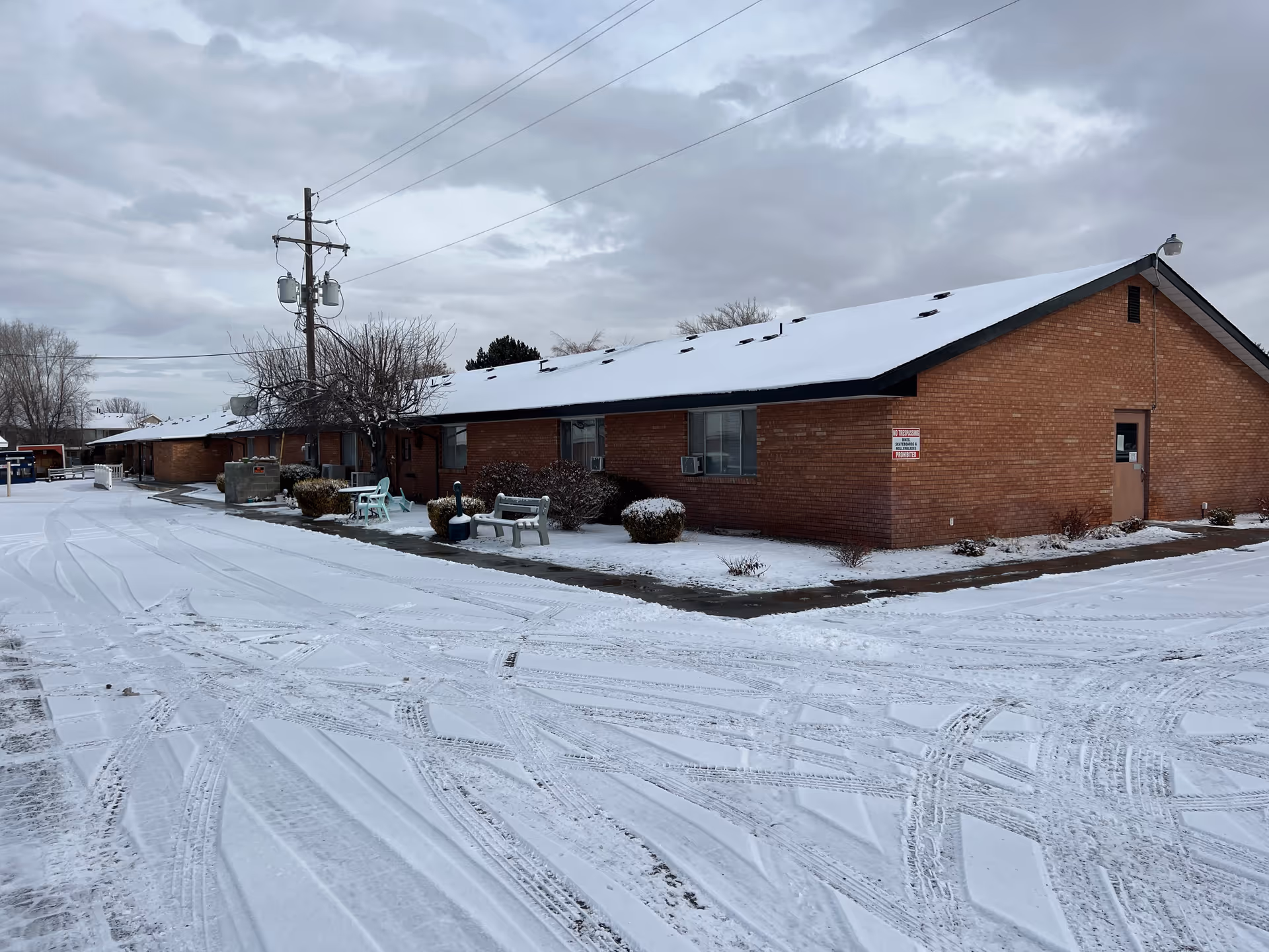 Brick, single-story building with snow-covered ground and outdoor seating along the front.
