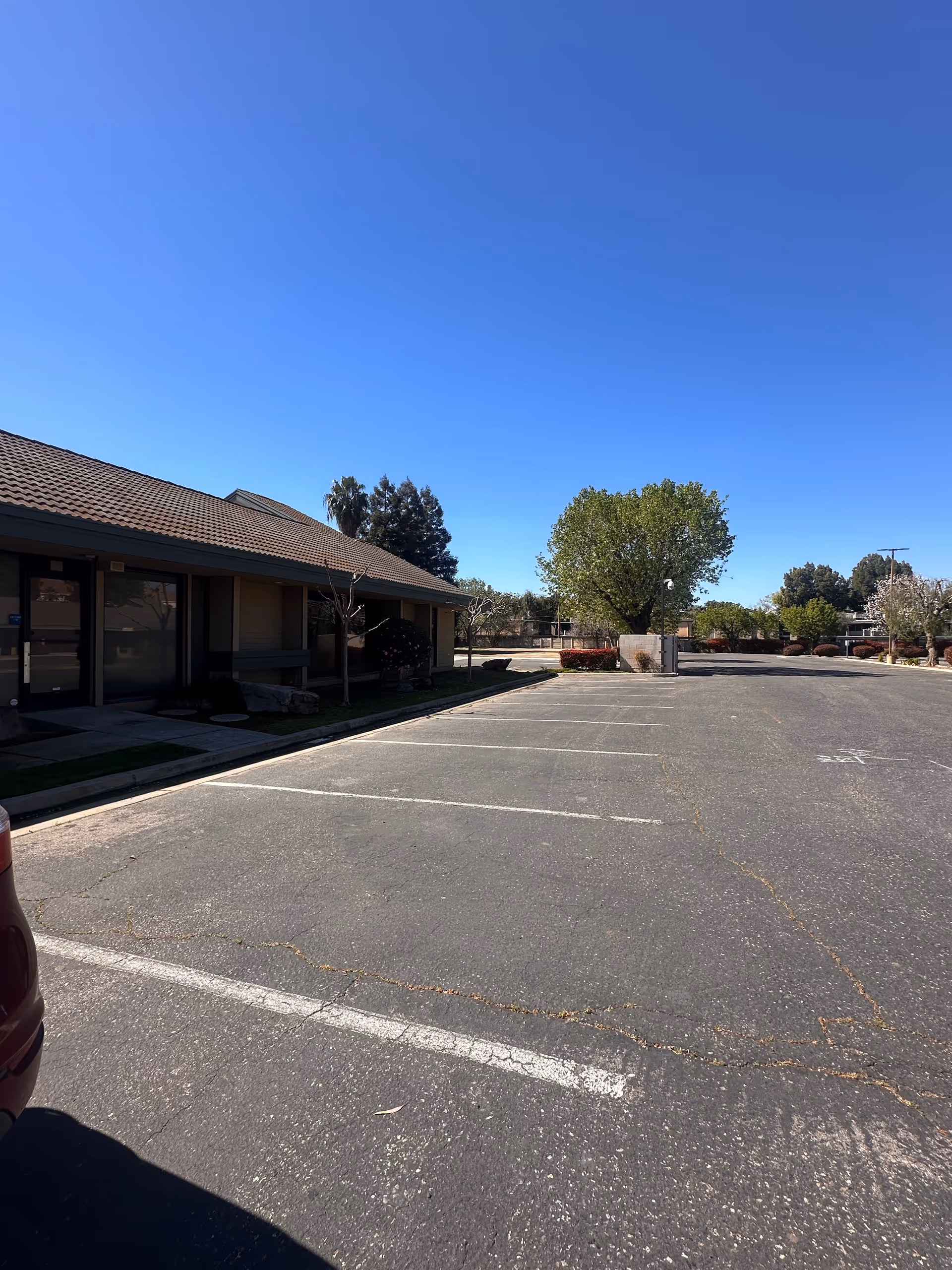 Single-story building exterior with a spacious parking lot under a clear blue sky.