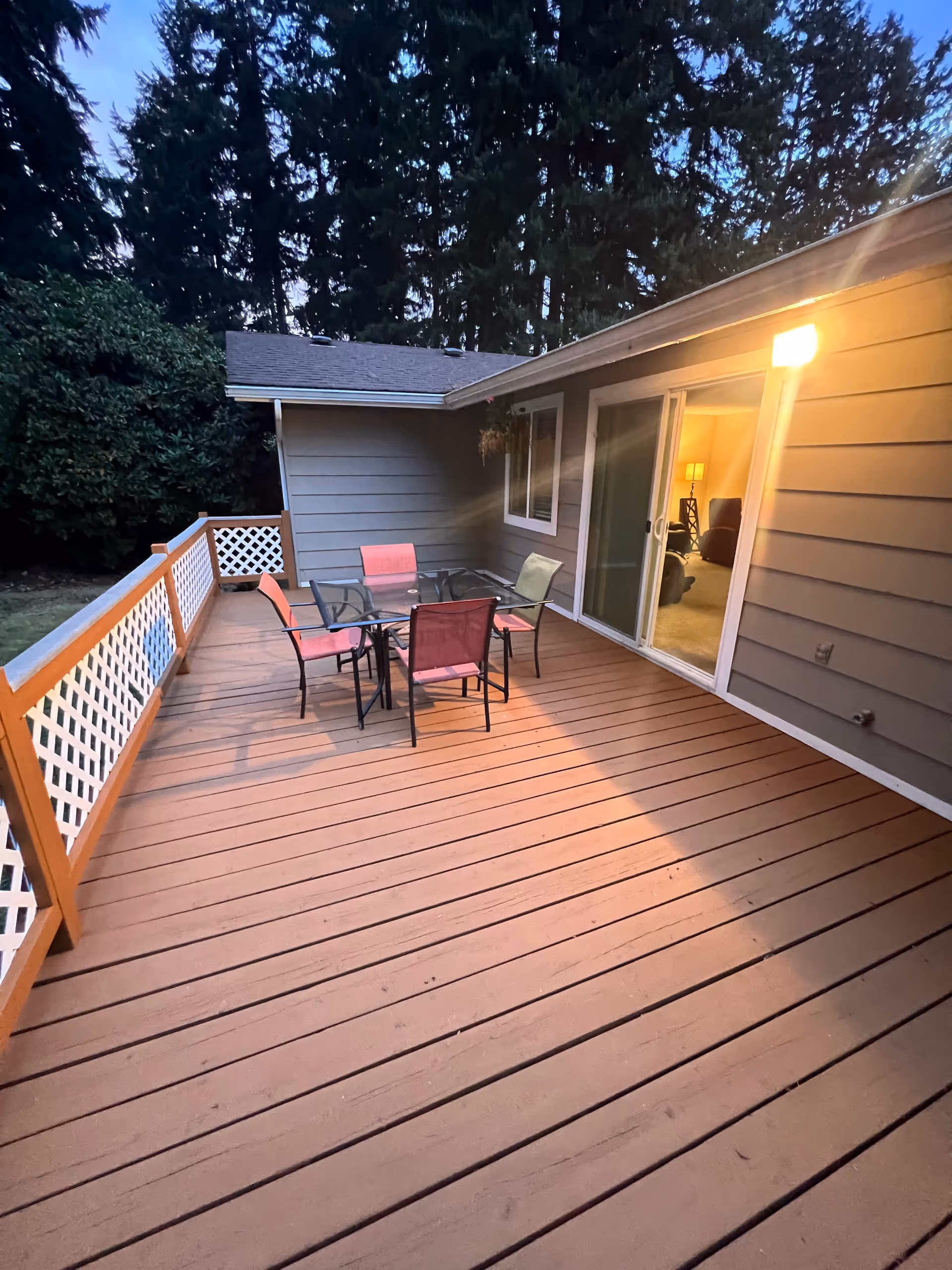 A wooden deck features a glass table and colorful chairs outside sliding doors.