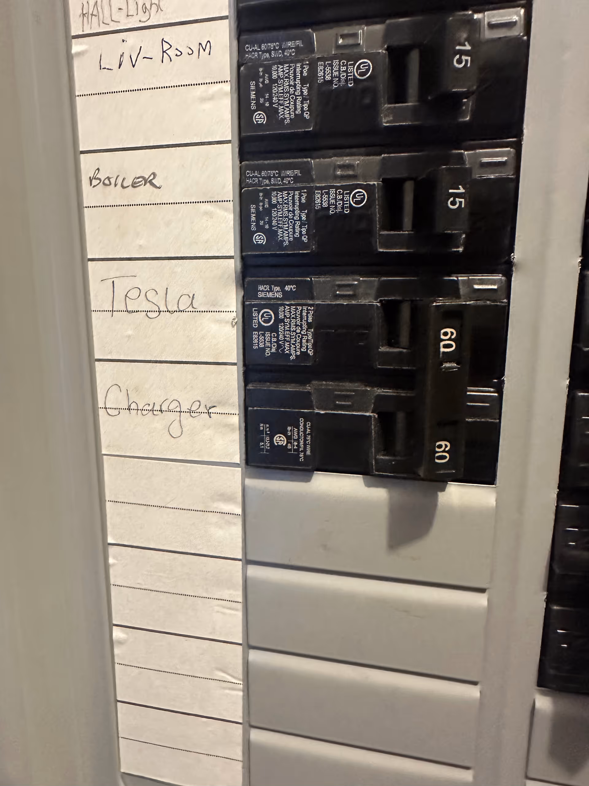 Close up of a circuit breaker panel with handwritten room labels.