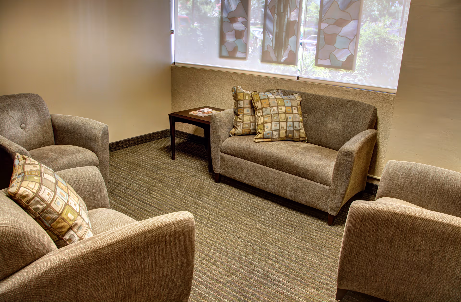 Cozy waiting area with gray couches, patterned cushions, and a small table by windows