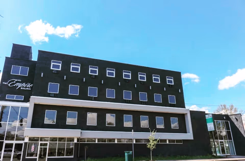 Front facade of a dark, modern building with many windows under a blue sky.