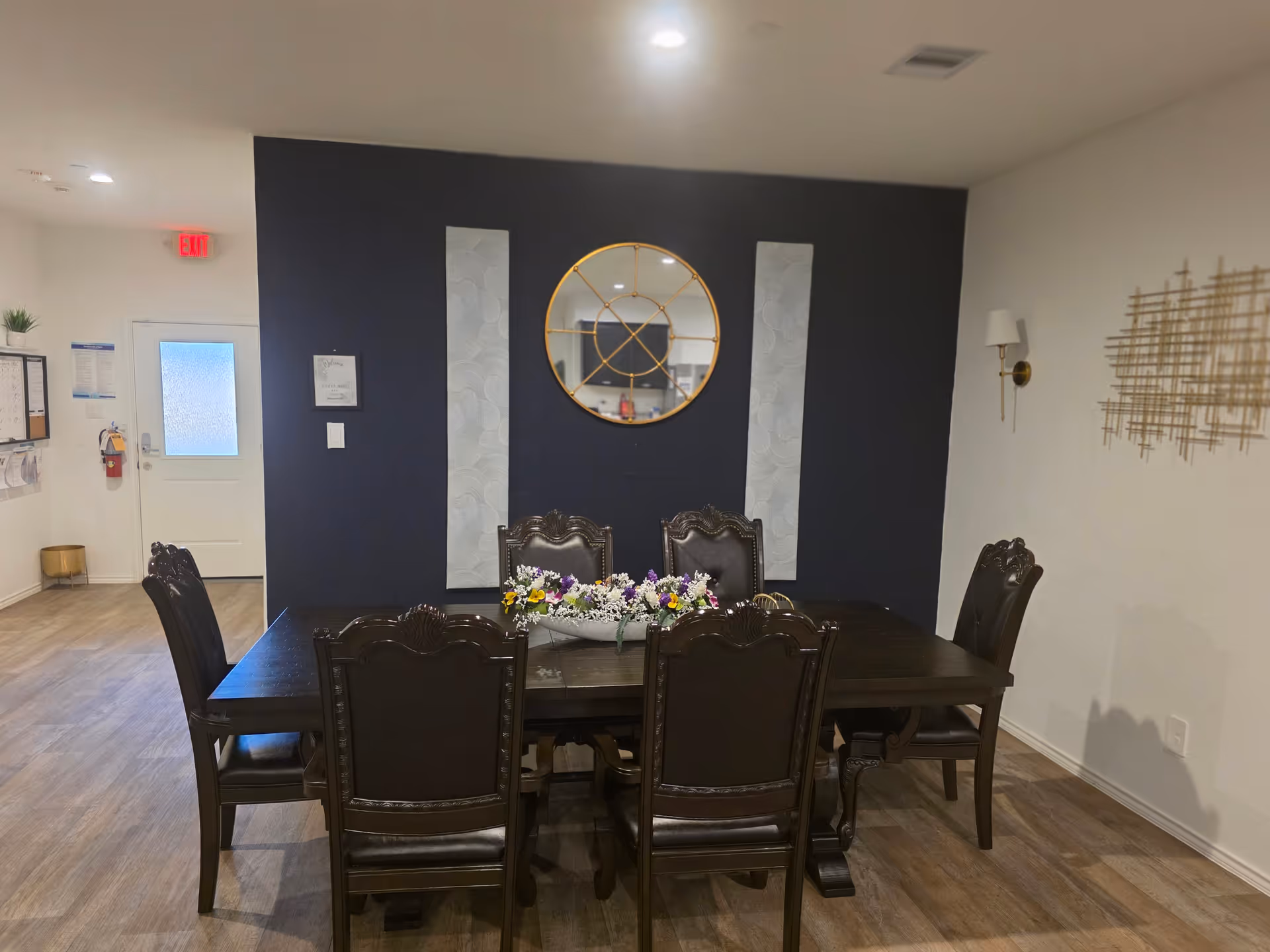 Dark wood dining table with six chairs and flower centerpiece against a navy accent wall.