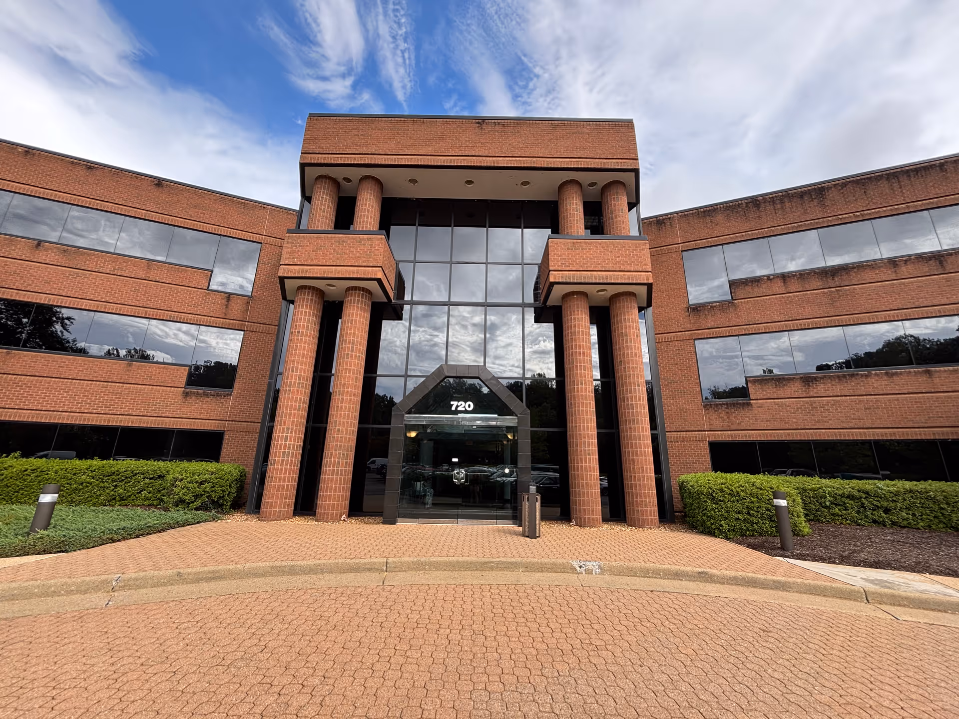 Red brick building with a central glass entry and tall supporting columns.
