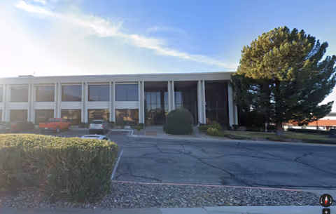 Front exterior of a two-story senior care facility with parked cars and landscaped shrubs.