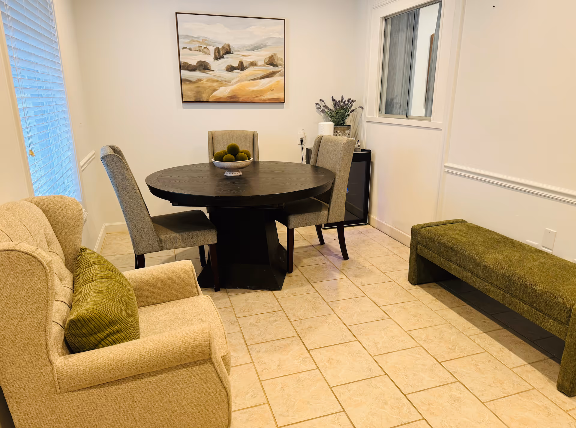 A senior living dining area with a round table, chairs, beige sofa, and a green bench.