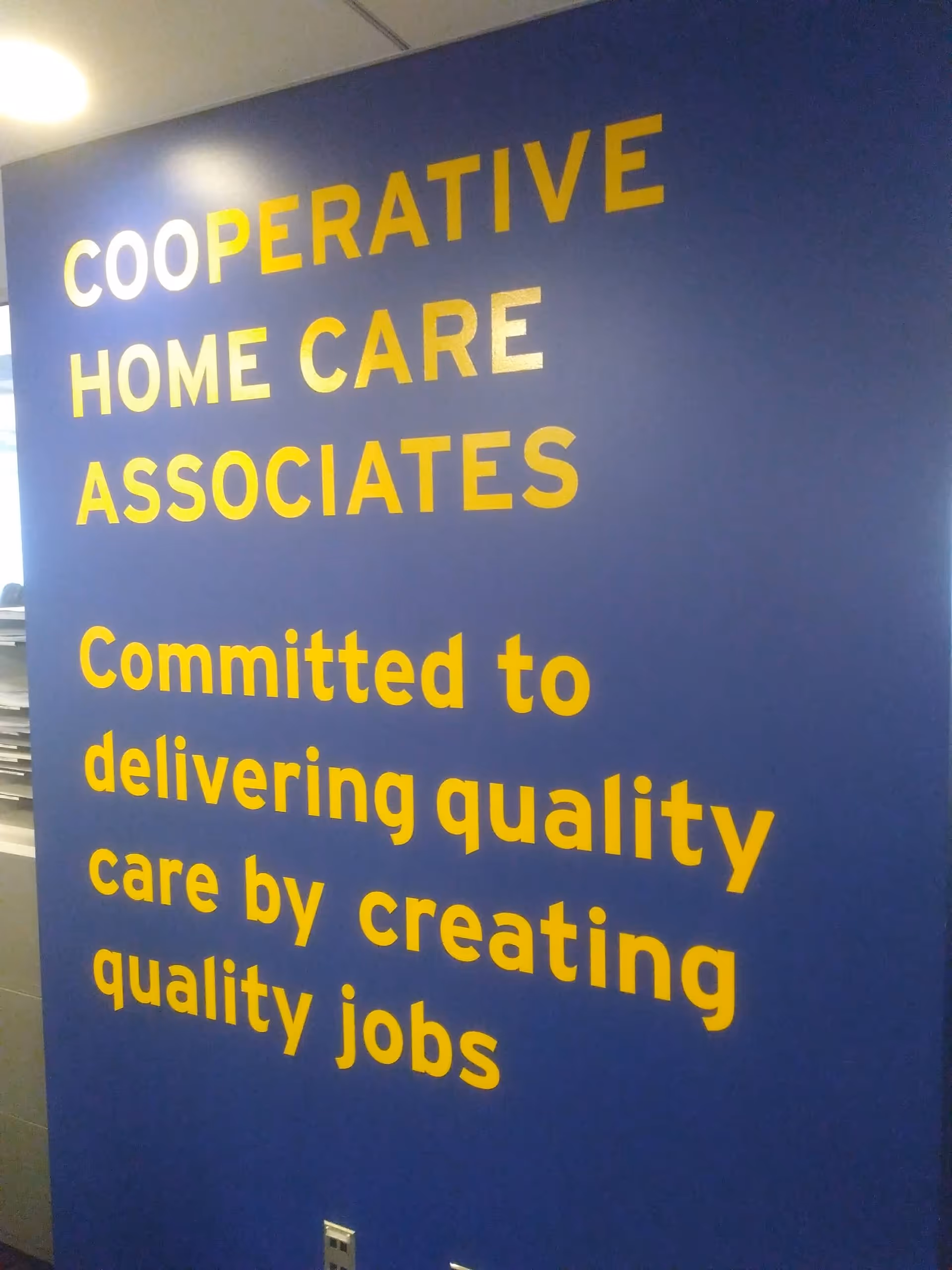 Blue interior wall with large yellow text displaying Cooperative Home Care Associates mission statement.