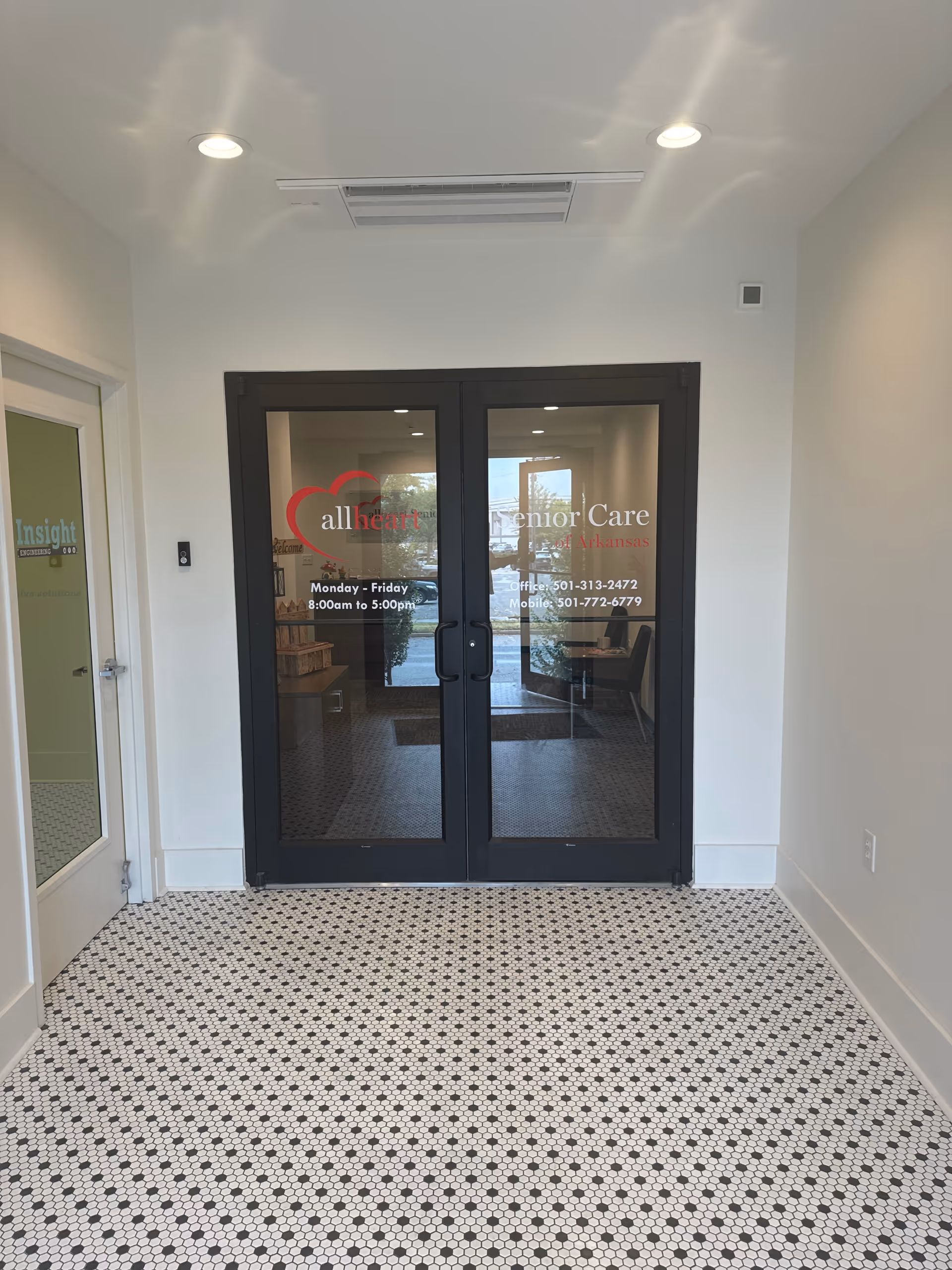 Double glass doors with allheart Senior Care branding, white walls, patterned tile floor, ceiling lights.