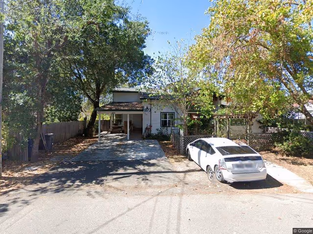 Two-story house with a car parked in the driveway and trees shading the front yard.