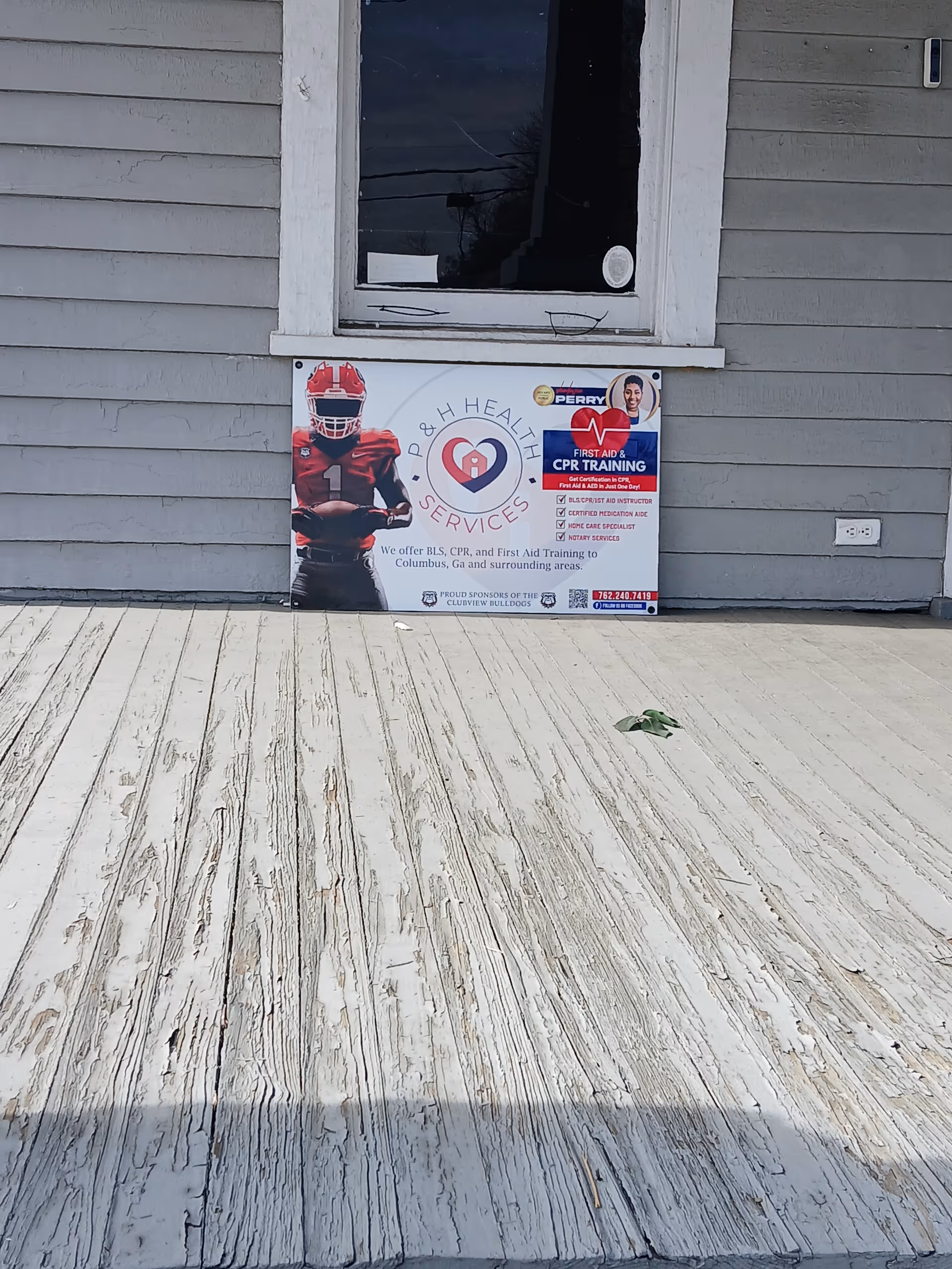 Exterior view of a gray building with a CPR training poster on a wooden front porch.