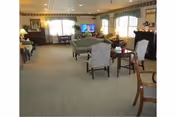 A spacious senior living lounge with chairs, tables, and a television.