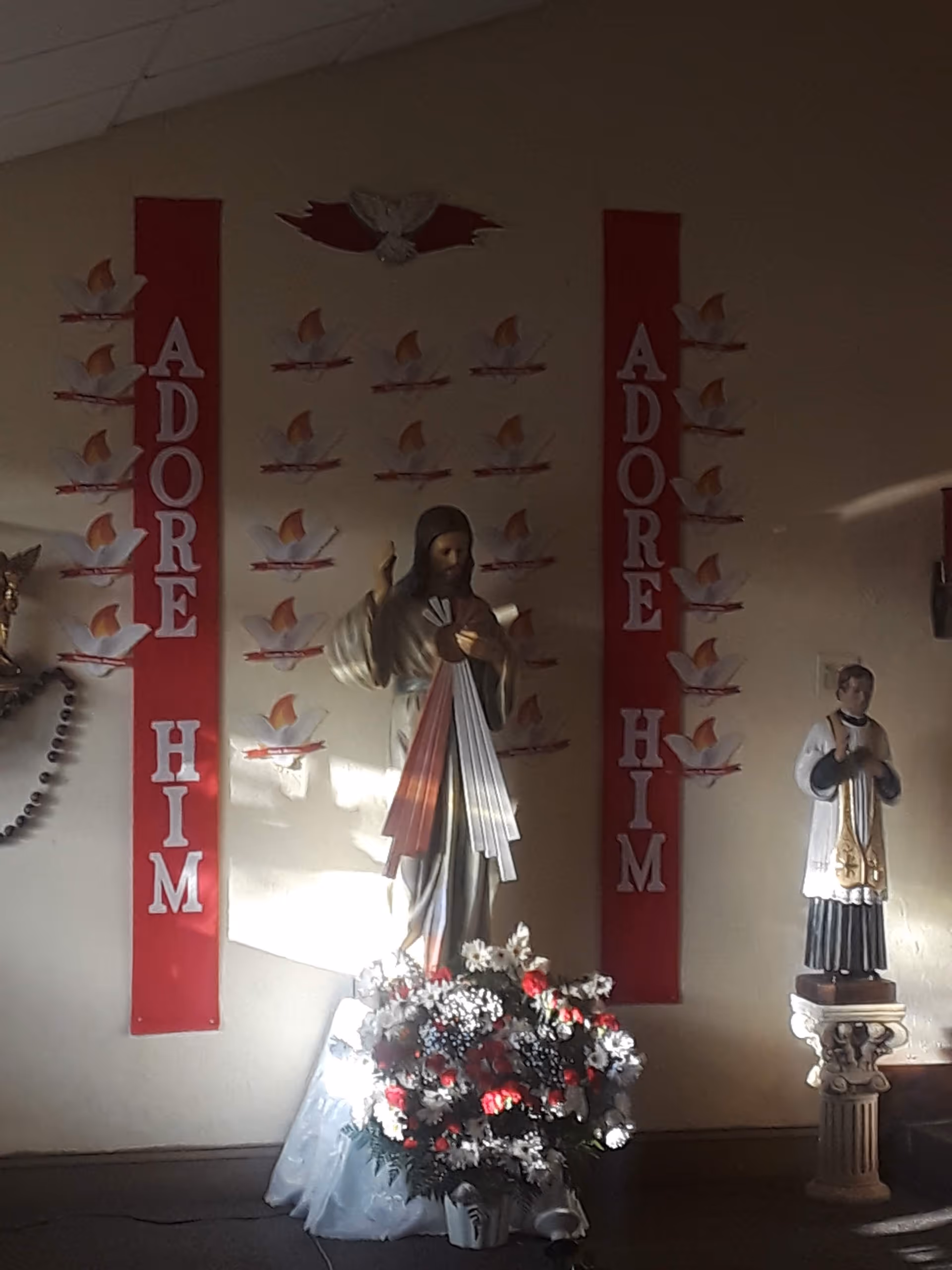 An interior display at Blessed Sacrament Manor with statues and red banners reading ADORE HIM.
