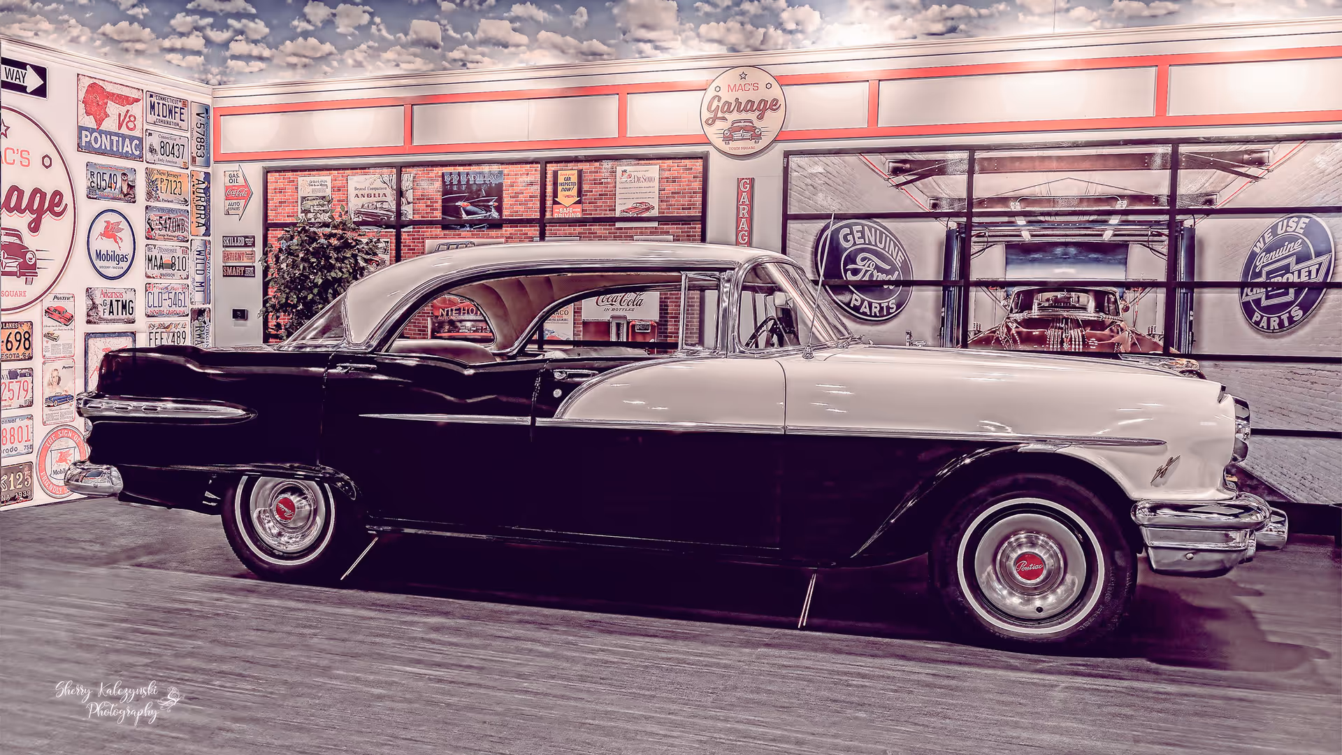 A vintage two-tone black-and-white classic car displayed inside a retro garage showroom with signs on the walls.