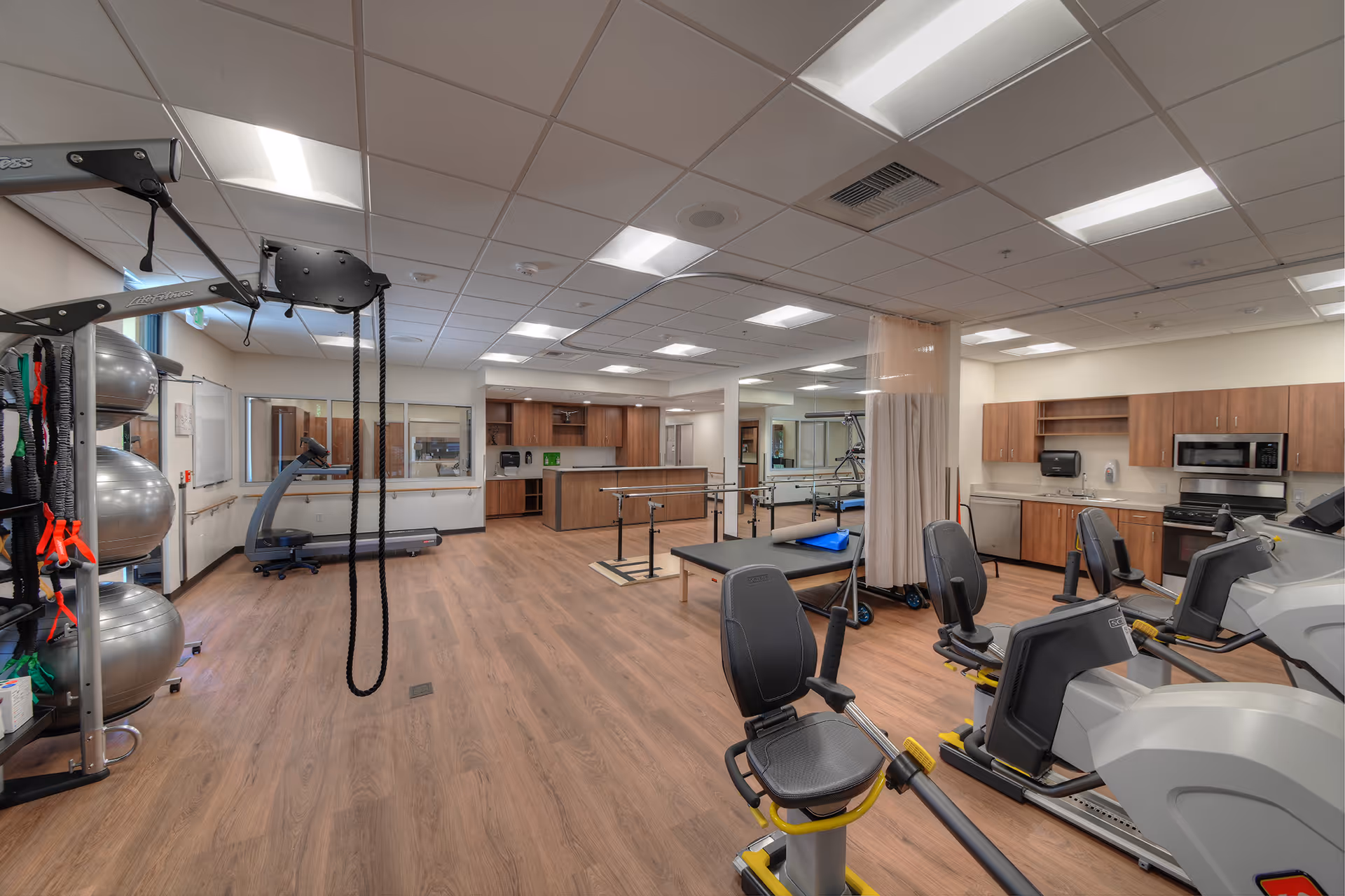 Spacious rehabilitation gym with treadmills, bikes, mats, and weights in a senior facility.
